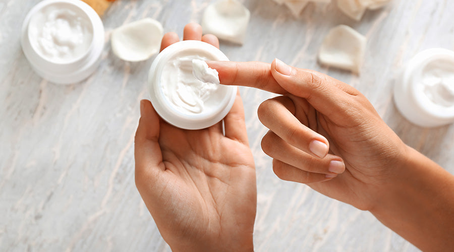 main qui tient un pot de crème fond clair avec d'autres pots ouverts