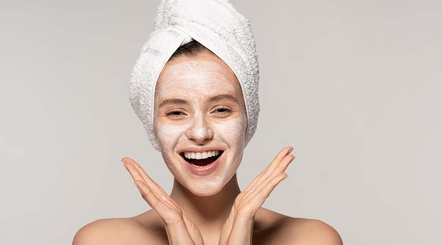 Femme souriante avec un masque exfoliant sur le visage, illustrant les bienfaits revitalisants et purifiants des soins gommants bio de IUM Paris.