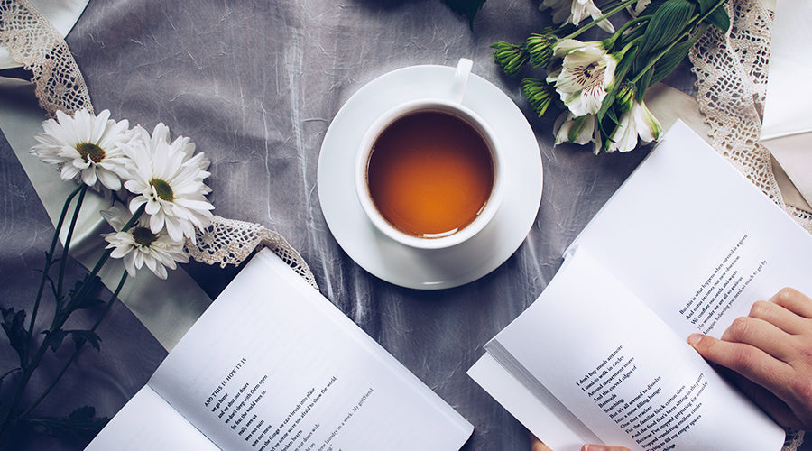 tasse de thé sur un lit entourée de fleurs et de livres