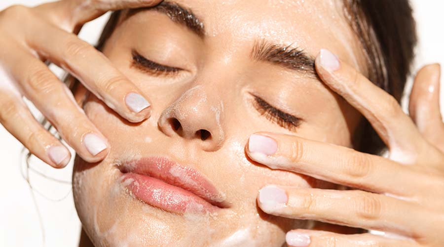 Zoom sur le visage d'une belle femme de face qui se nettoie la peau en fermant les yeux