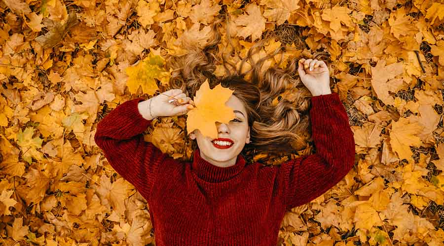 Jeune femme souriante avec un pull rouge vue de haut sur un tas de feuilles d'automne oranges