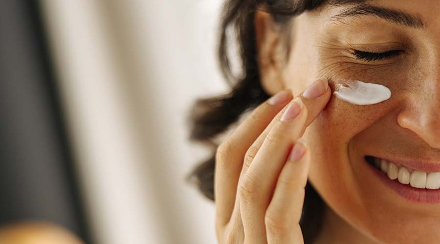 femme brune souriante avec de la crème sous les yeux pour estomper cernes 