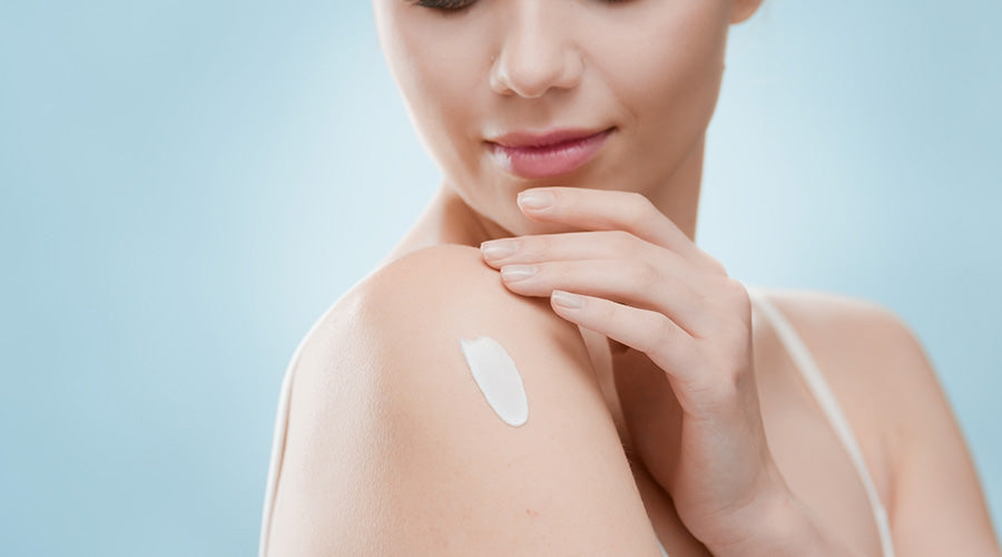 Belle femme applique de la crème ium naturelle et bio sur son épaule sur fond bleu