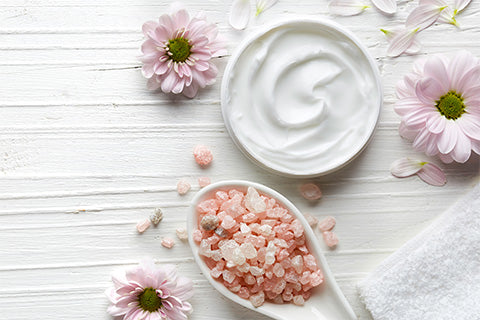 cuillère de cristaux de potassium vue de haut à coté d'un pot de crème ium et des fleurs violettes