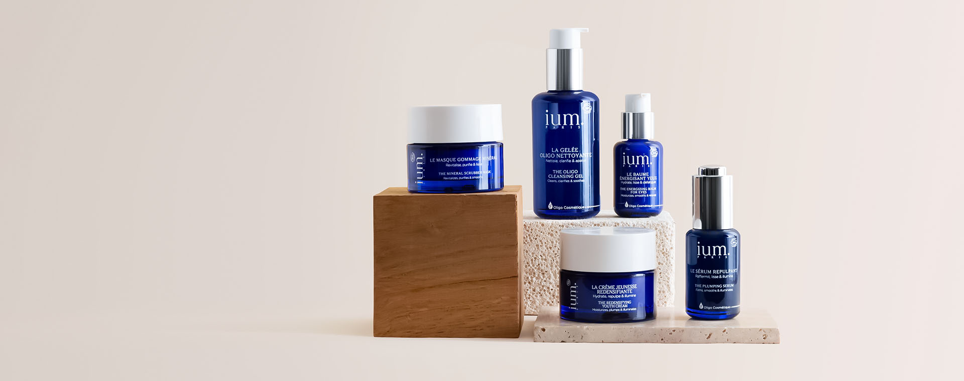 Collection complète de soins visage bio IUM Paris sur fond beige, comprenant crème jeunesse, sérum repulpant, gelée nettoyante, masque gommage et baume énergisant yeux.