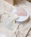 Pierre de massage Gua Sha en Quartz rose et sa pochette en coton blanc sur du marbre beige