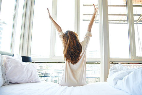 Femme de dos se réveille en étirant ses bras après un sommeil réparateur pour la peau